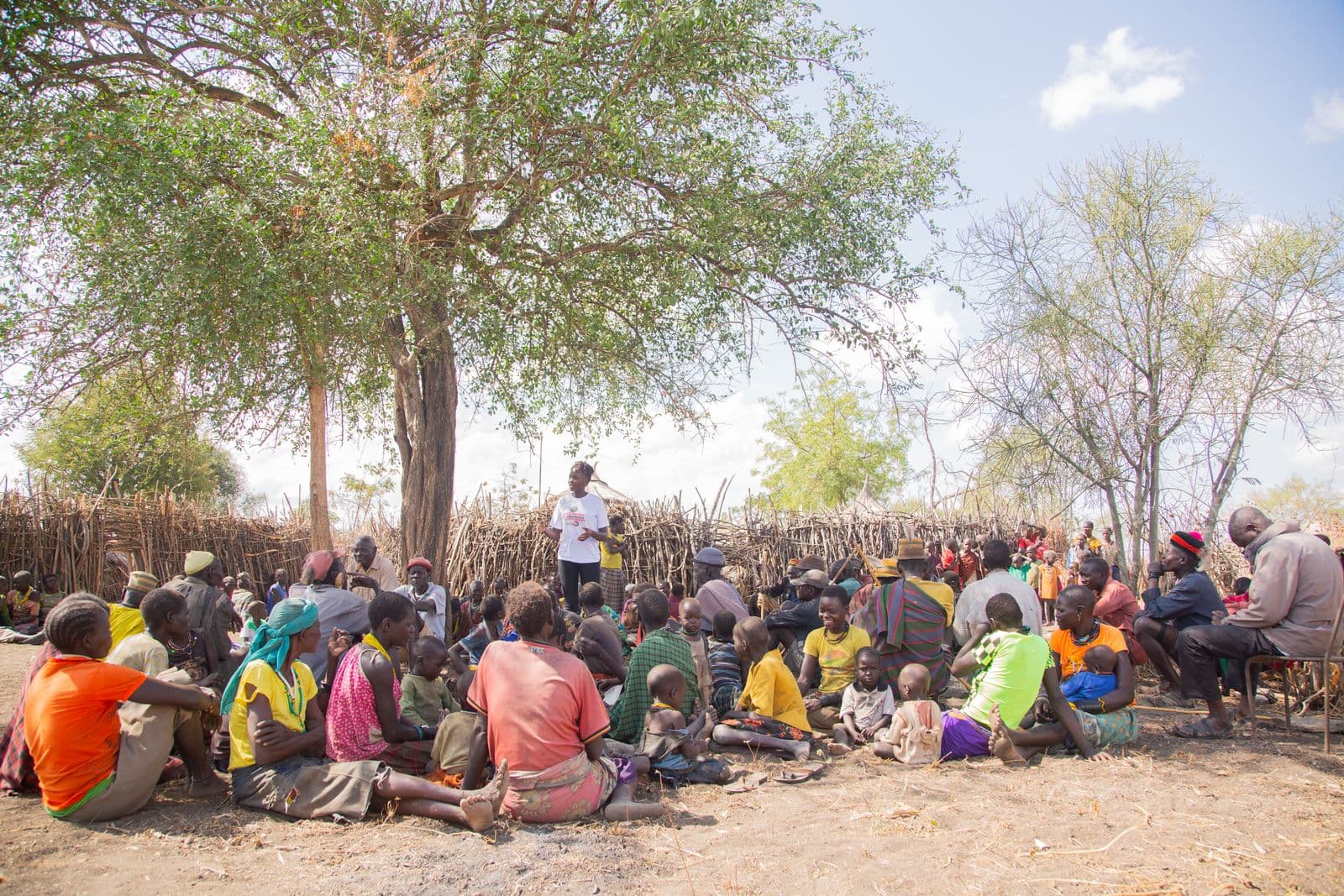 A facilitator addresses a community gathered outdoors for a grassroots outreach session